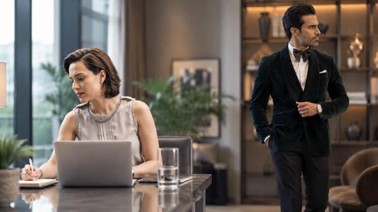 Woman seated at a desk and man standing apart in a modern interior, illustrating emotional separation and child support responsibilities after divorce.