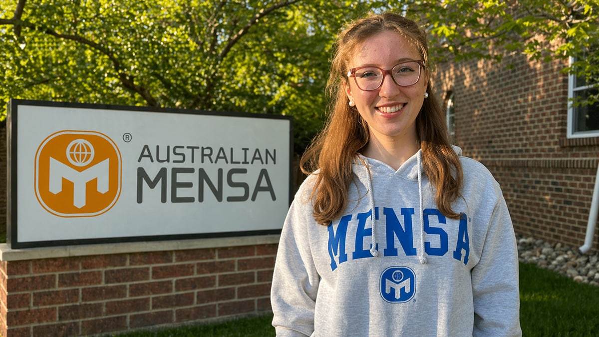 Young student in a Mensa hoodie standing outdoors beside an Australian Mensa sign, representing gifted education support and pathways