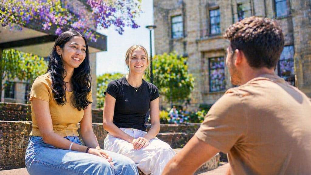 Three university students talking together in a courtyard at UQ St Lucia campus in Brisbane, illustrating typical uni life after school age when child support has ended