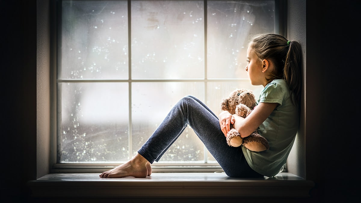 Girl holding teddy and looking out window